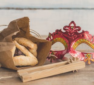 Purim jewish holiday composition with hamantaschen, purim mask and purim gragger on a vintage wood background with copy space