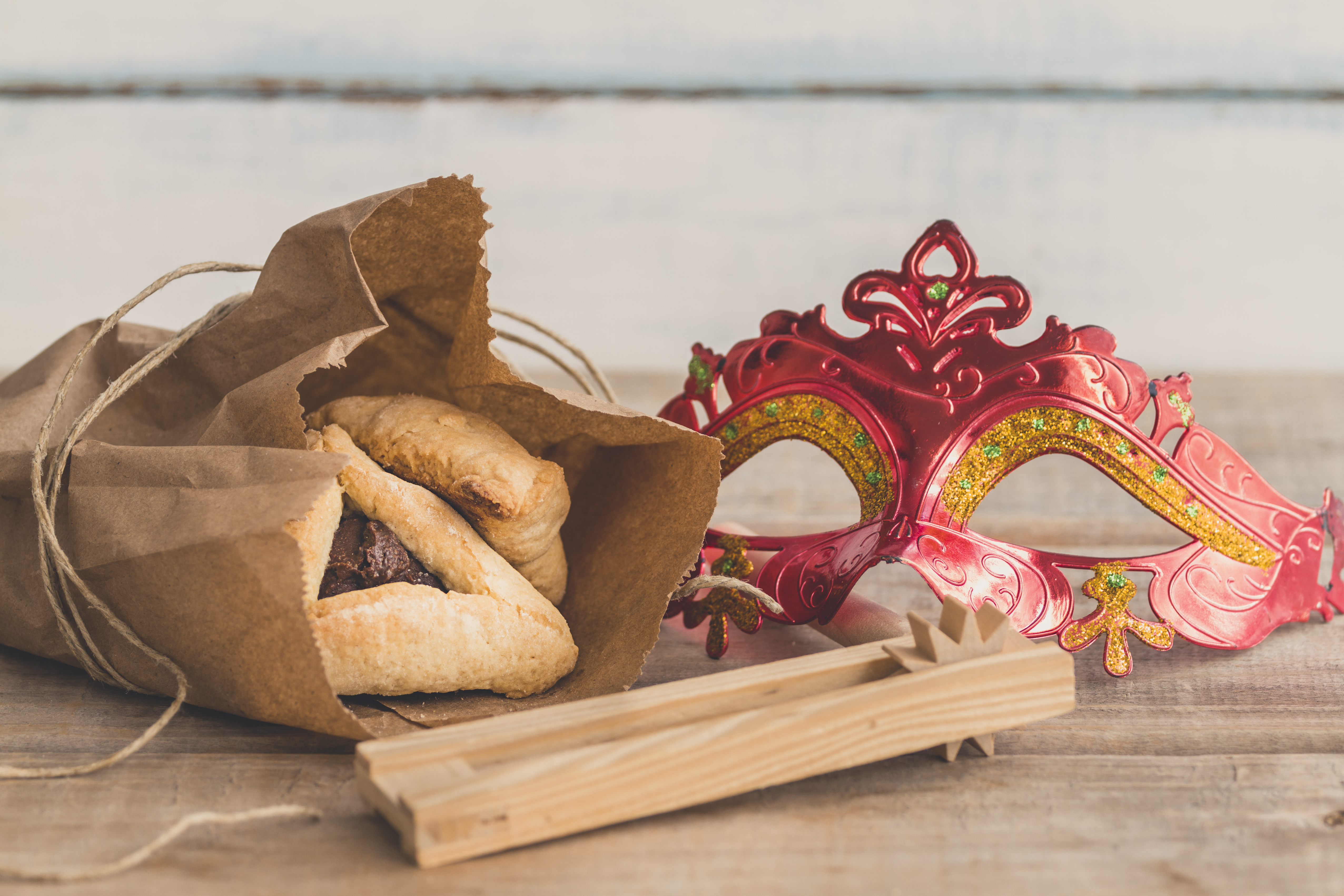 Purim jewish holiday composition with hamantaschen, purim mask and purim gragger on a vintage wood background with copy space