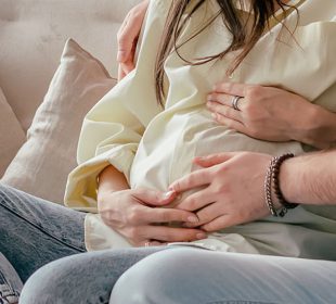 Couple on couch with hands on pregnant stomach
