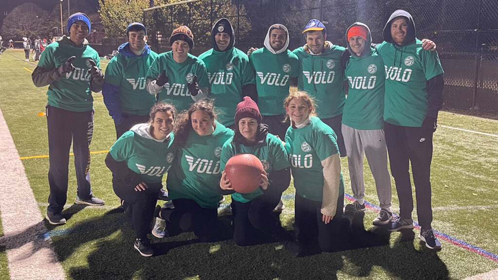 Group photo of kickball team members in green jerseys on a playing field at night.