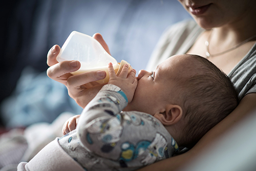 A baby lays in his mother's arms while drinking from a baby bottle.