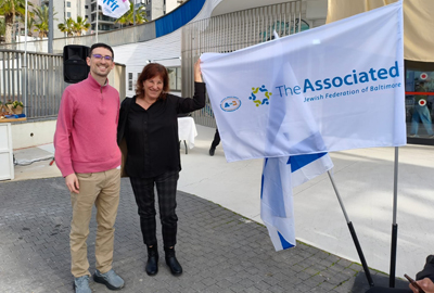 Jason Horowitz and Sigal Ariely with The Associated flag outside of building