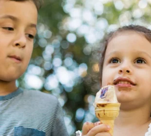 Group of children sitting in a row and eating ice cream cone in nature