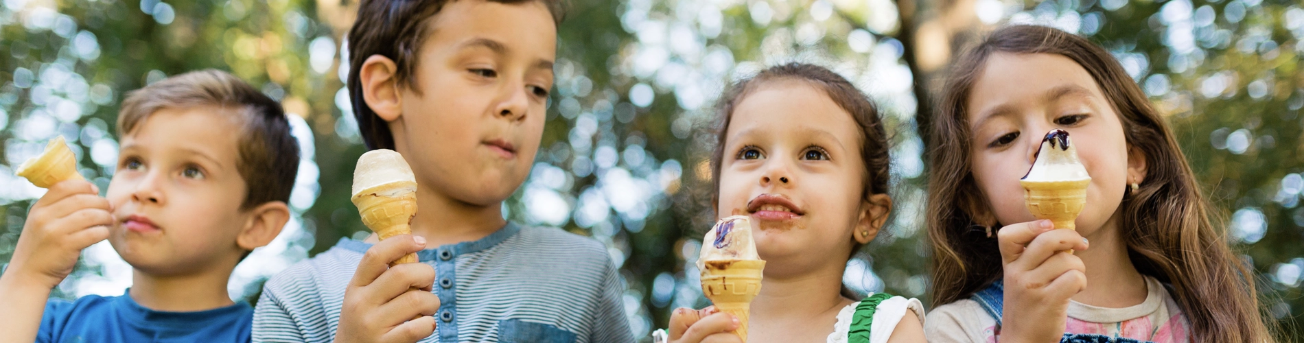 Group of children sitting in a row and eating ice cream cone in nature